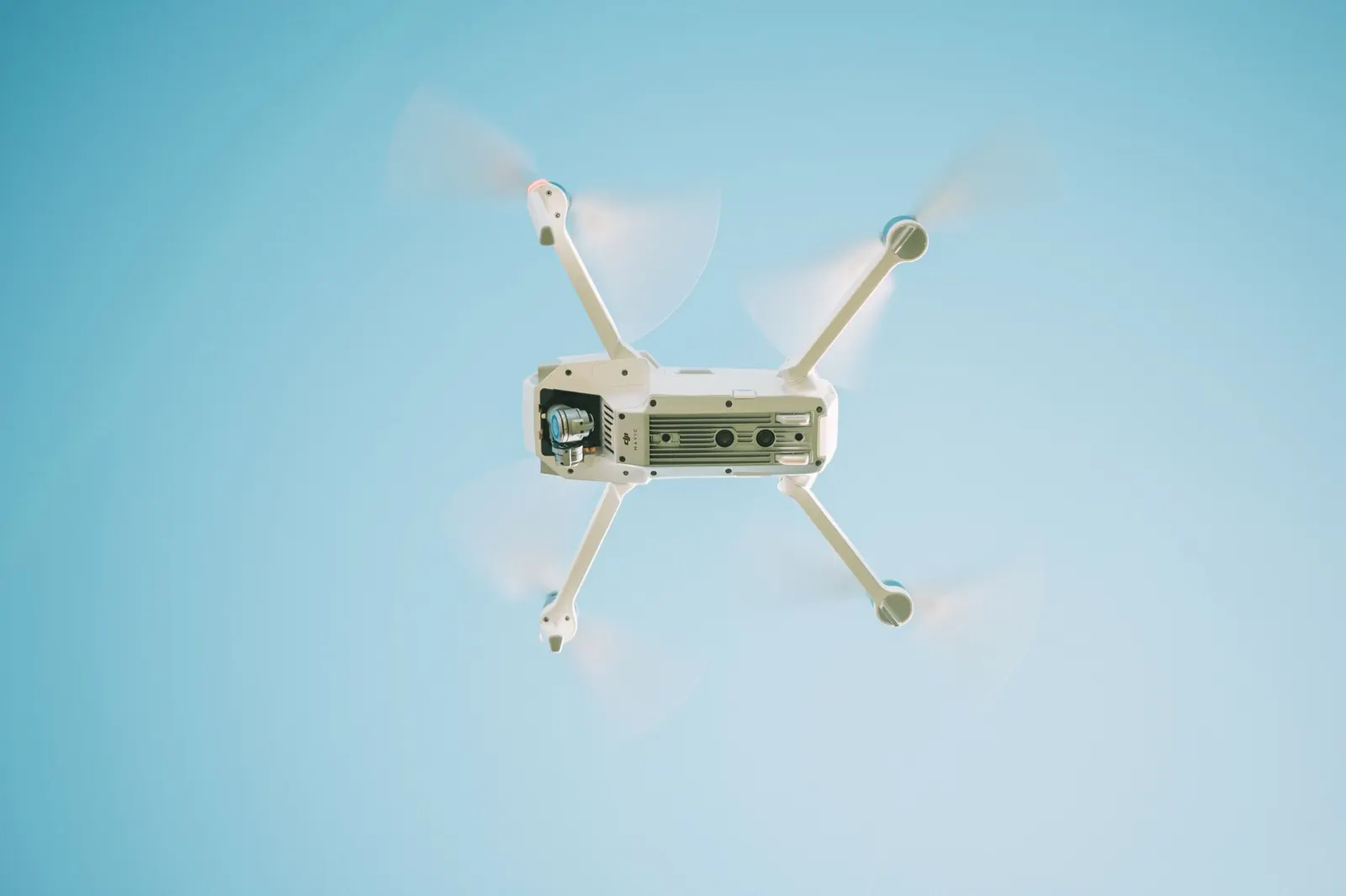 A sleek white drone flying under a clear blue sky, capturing aerial views.